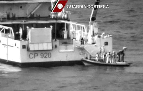 Italian coast guard officers stand on a dinghy beside an Italian coast guard vessel as a massive search and rescue operation is conducted at sea after a boat carrying migrants capsized overnight, in this still image taken from video April 19, 2015. As man