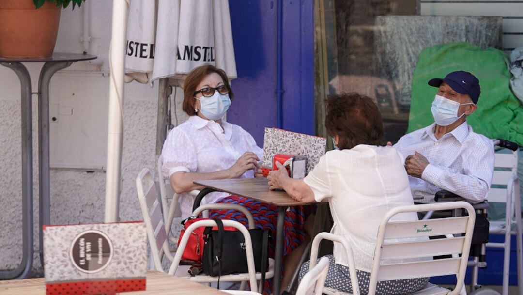 Ancianos con mascarilla conversan sentados en la terraza de un bar.