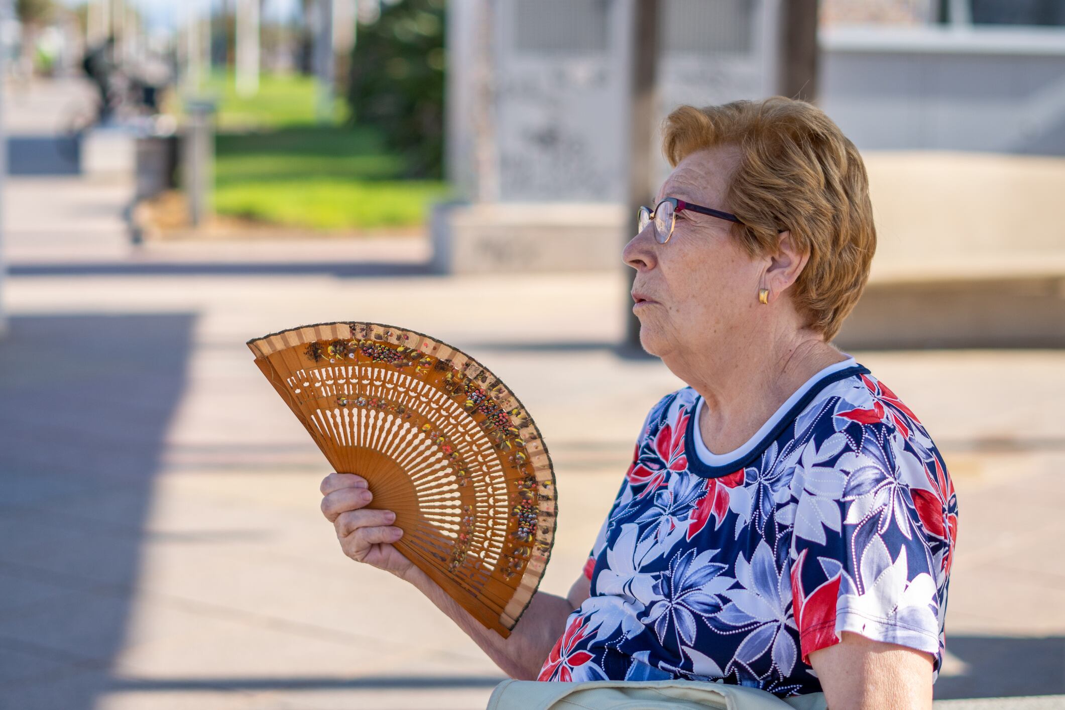 Mujer abanicándose, sentada en un banco en la calle