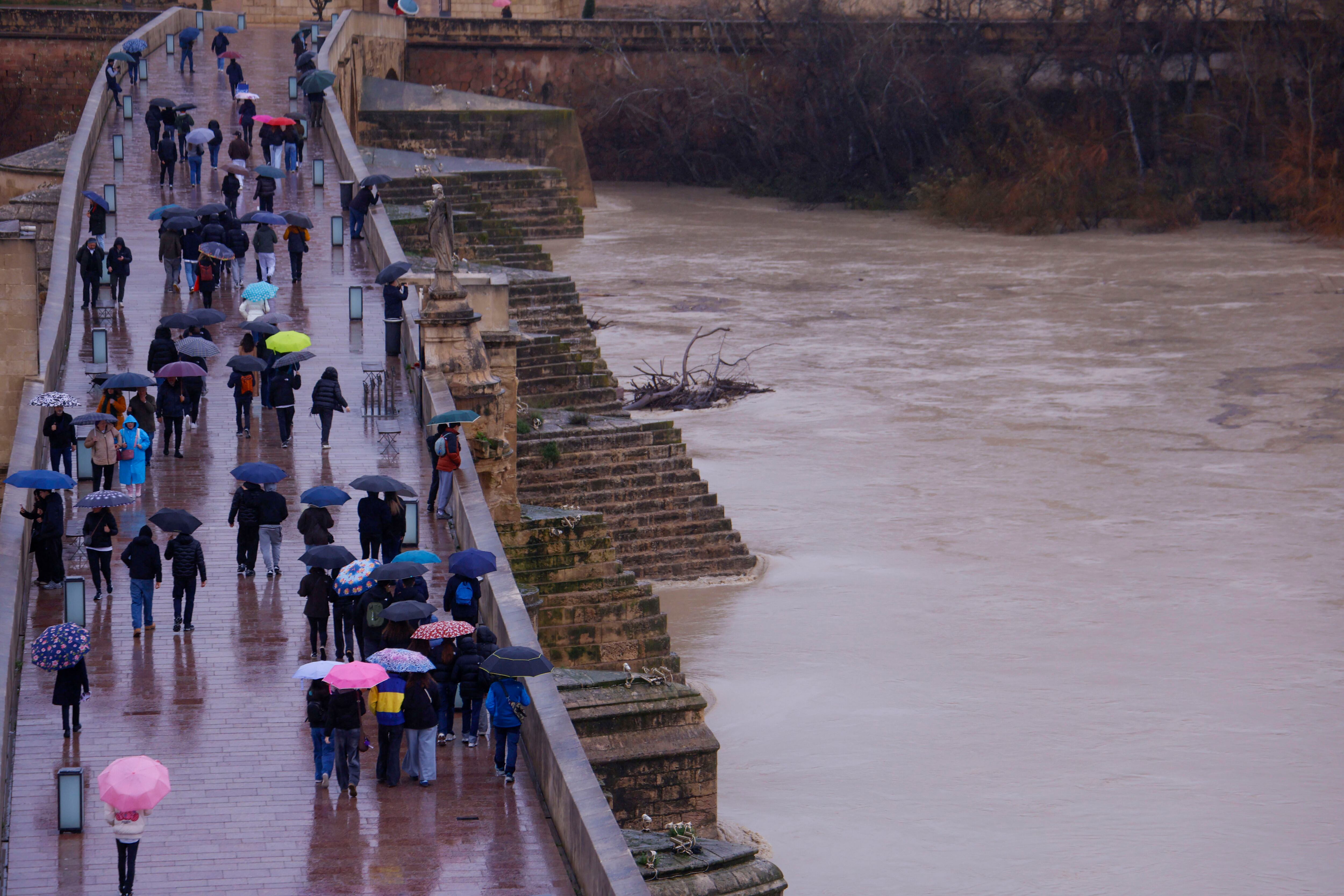 Varias personas cruzan por el puente sobre el río Guadalquivir que ha alcanzado el umbral naranja a su paso por Córdoba