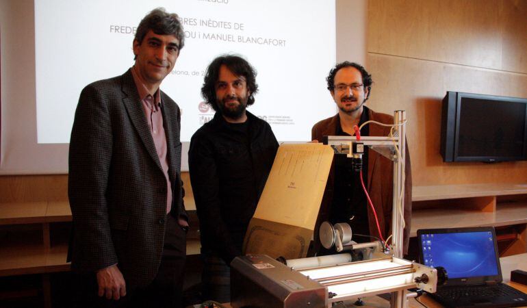 El director del Museu de la Música, Jaume Ayats, l'investigador Jordi Roquer i el director del Grup de Recerca MUSC (UAB), mostren un rotlle de pianola davant l'escaner Pianola Roll Digitizer