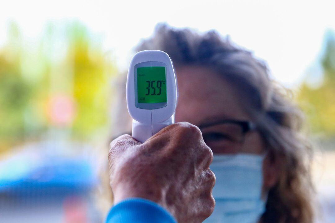 Un sanitario le toma la temperatura a una mujer antes de realizarle un test de antígenos