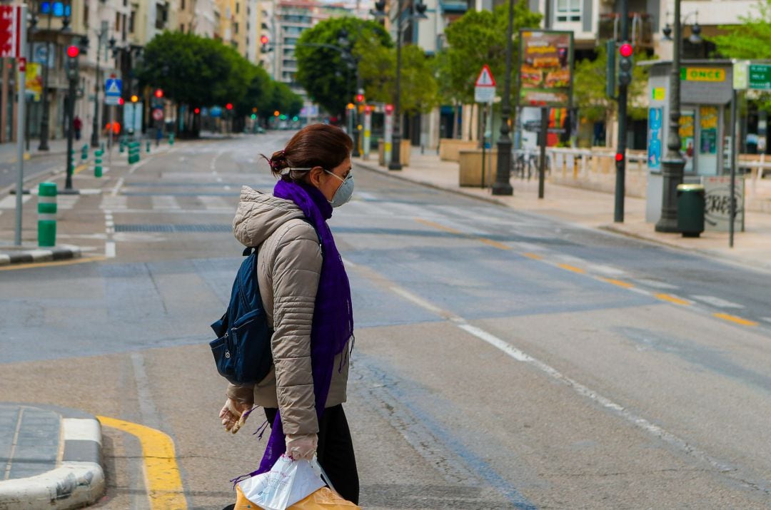 Una mujer protegida con mascarilla sanitaria camina por una de las calles desiertas de València