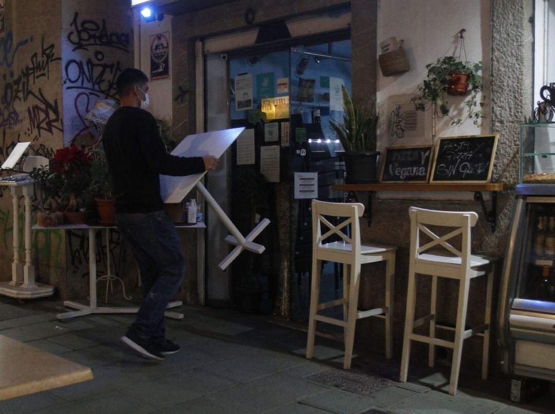 Un camarero recoge las mesas de la terraza de una cafetería.