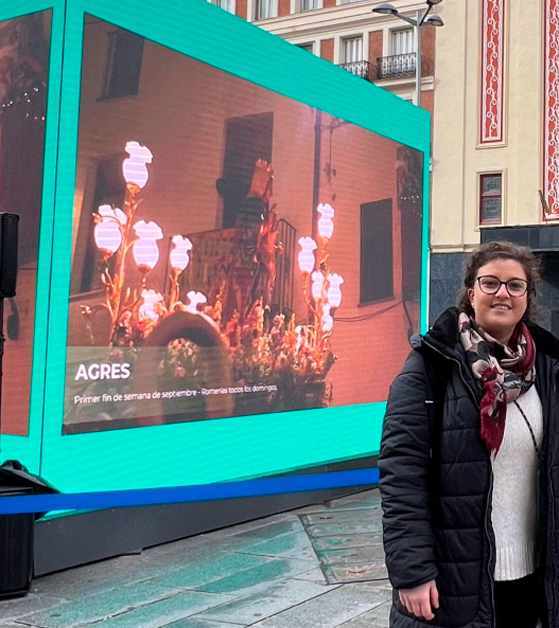 La alcaldesa de Agres, María García, junto al cubo ubicado en la plaza Callao de Madrid con un imagen de la Mare de Déu de la localidad