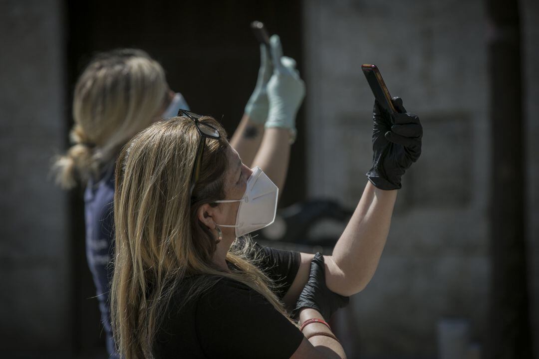 Dos personas protegidas con mascarillas y guantes graban con sus móviles  durante el estado de alarma. 