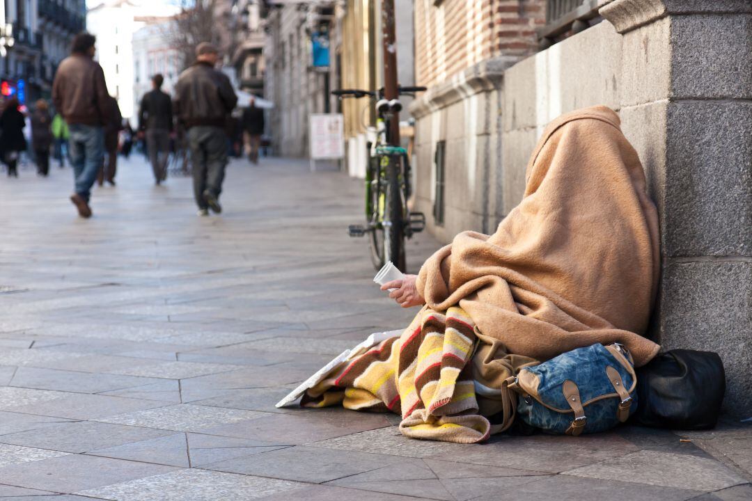 Un hombre cubierto por unas mantas sujeta un vaso de plástico en la calle Arenal de Madrid.