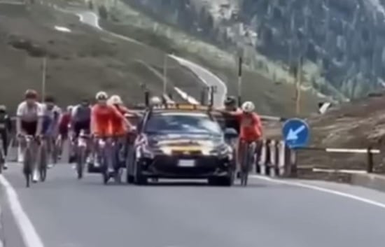 Varios ciclistas se agarran a un coche durante el Giro de Italia sub-23