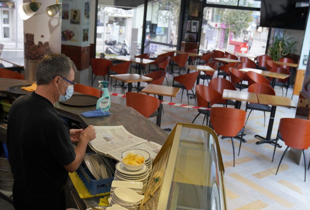 Un camarero lee un periódico en el interior de su bar.