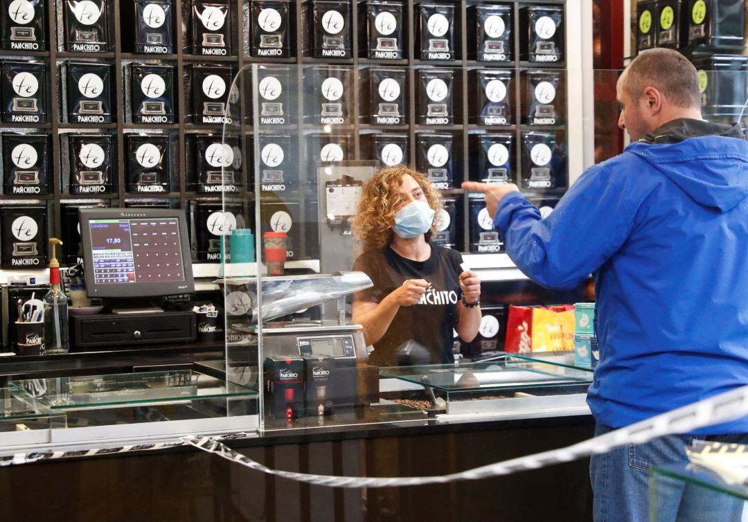 Una dependienta atiende a un cliente tras una mampara de separación en un comercio de San Sebastián.
