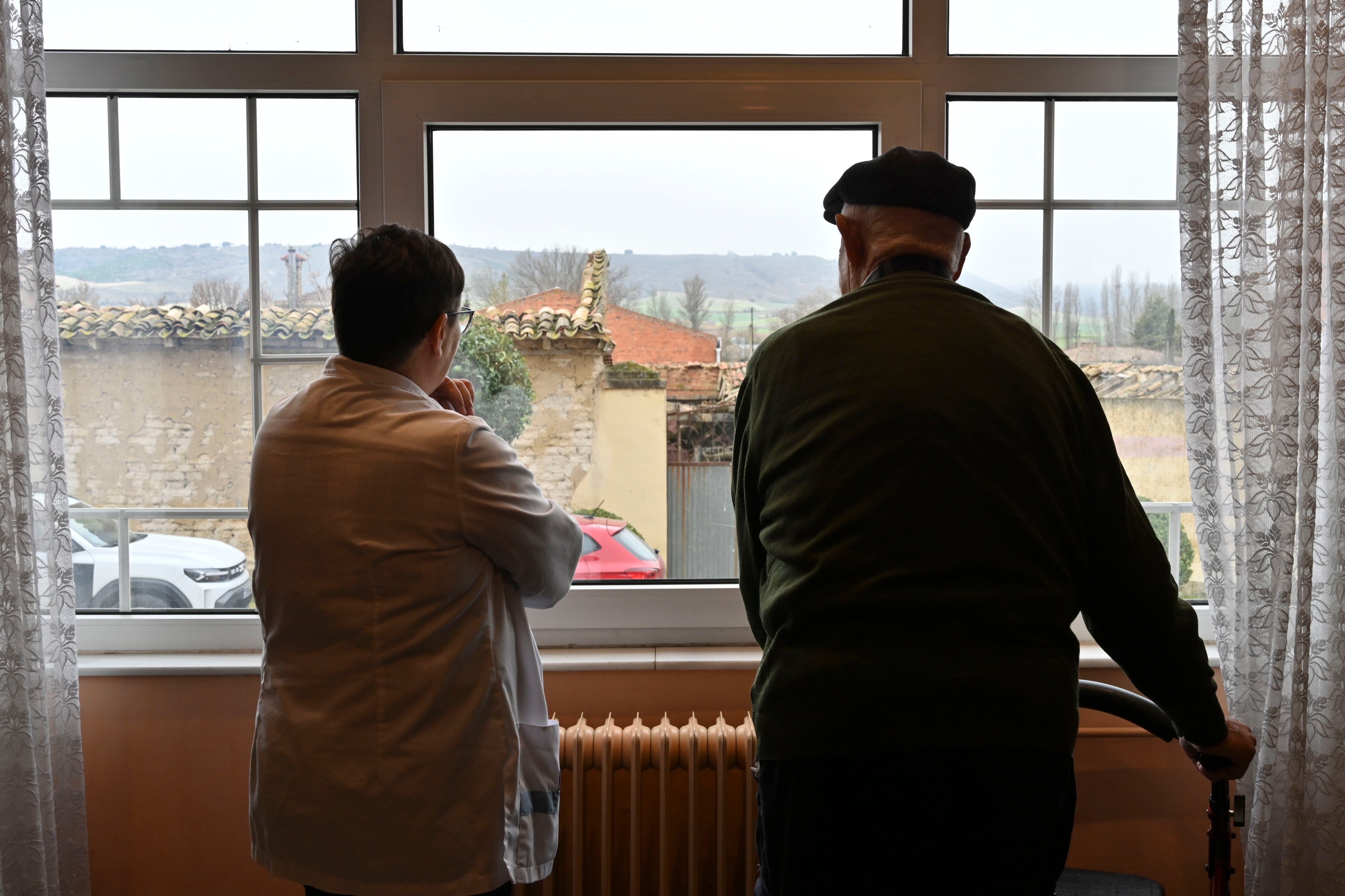 CEVICO DE LA TORRE (PALENCIA), 27/02/2025.- Luis Merino (i), de 98 años, uno de los primeros vacunados contra el Covid en Castilla y León y Mari Bilbao (d) supervisora de la residencia de Cevico de la Torre, miran por la ventana como hacían aquellos días de 2020. Hace cinco años, cuando se notificaron los dos primeros casos de covid en Castilla y León, la incertidumbre y el miedo se instaló en la sociedad ante este virus desconocido para el que no había vacuna. Diez meses más tarde el avance de la ciencia y la investigación permitió poner las primeras dosis en la Comunidad. Fue en la residencia de mayores de Cevico de la Torre (Palencia), donde se empezó a ver la luz al final del túnel.-EFE/ Almudena Álvarez
