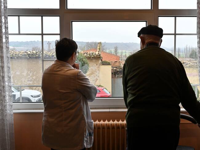 CEVICO DE LA TORRE (PALENCIA), 27/02/2025.- Luis Merino (i), de 98 años, uno de los primeros vacunados contra el Covid en Castilla y León y Mari Bilbao (d) supervisora de la residencia de Cevico de la Torre, miran por la ventana como hacían aquellos días de 2020. Hace cinco años, cuando se notificaron los dos primeros casos de covid en Castilla y León, la incertidumbre y el miedo se instaló en la sociedad ante este virus desconocido para el que no había vacuna. Diez meses más tarde el avance de la ciencia y la investigación permitió poner las primeras dosis en la Comunidad. Fue en la residencia de mayores de Cevico de la Torre (Palencia), donde se empezó a ver la luz al final del túnel.-EFE/ Almudena Álvarez