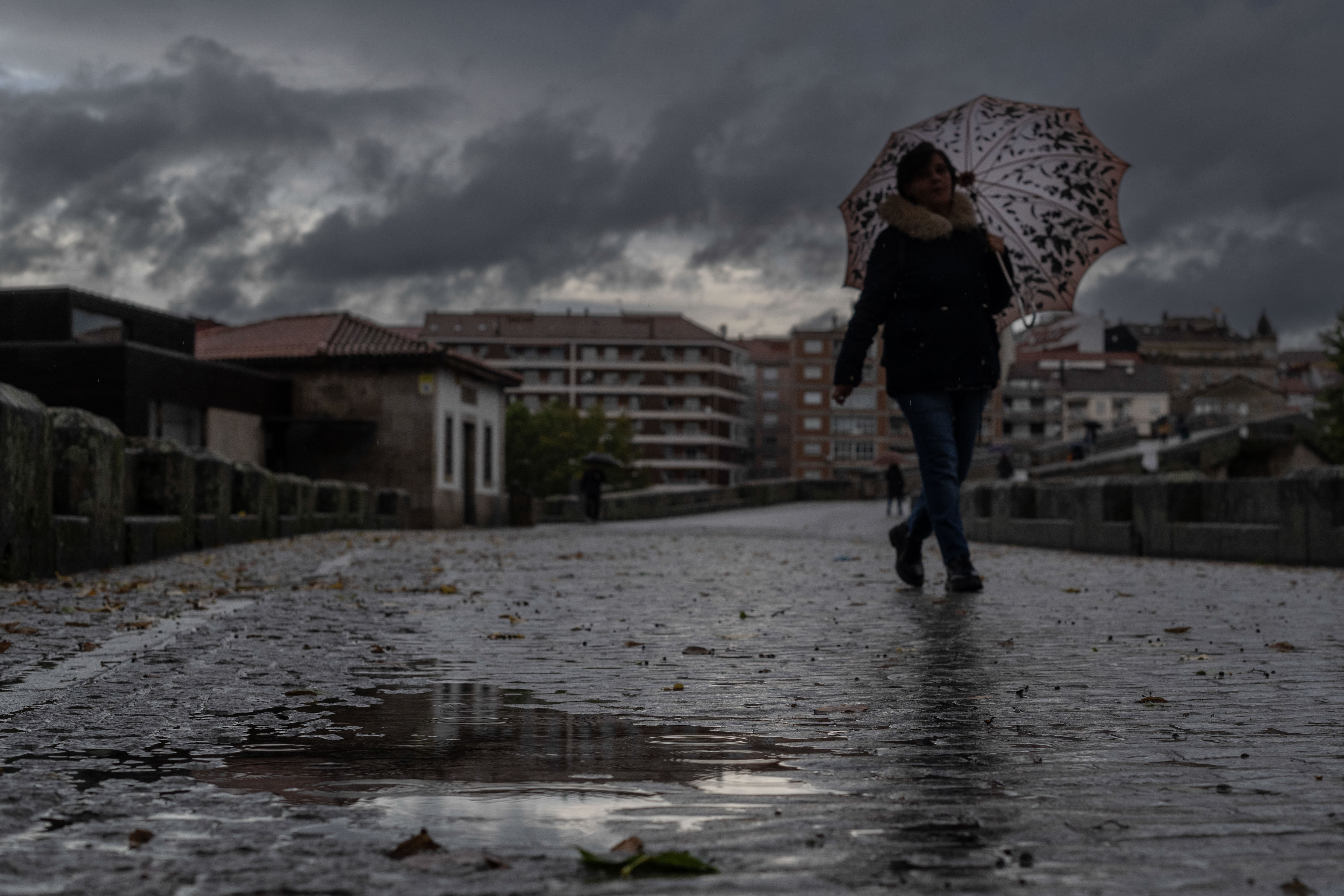 GRAF6115. OURENSE, 19/10/2022.- Una mujer se refugia de la lluvia con un paraguas mientras camina por el puente romano de Ourense, este miércoles. La llegada a la Península de la primera borrasca de gran impacto de la temporada dejará los próximos días &quot;importantes y generosas lluvias&quot; en amplias zonas del país, sobre todo del centro y mitad oeste peninsular. Dicha borrasca, &quot;bautizada&quot; con el nombre de Armand por el IPMA (servicio meteorológico portugués) será la primera de gran impacto de la nueva temporada 2022-2023 nombrada por el grupo del suroeste, en el que se encuadra España. EFE/ Brais Lorenzo
