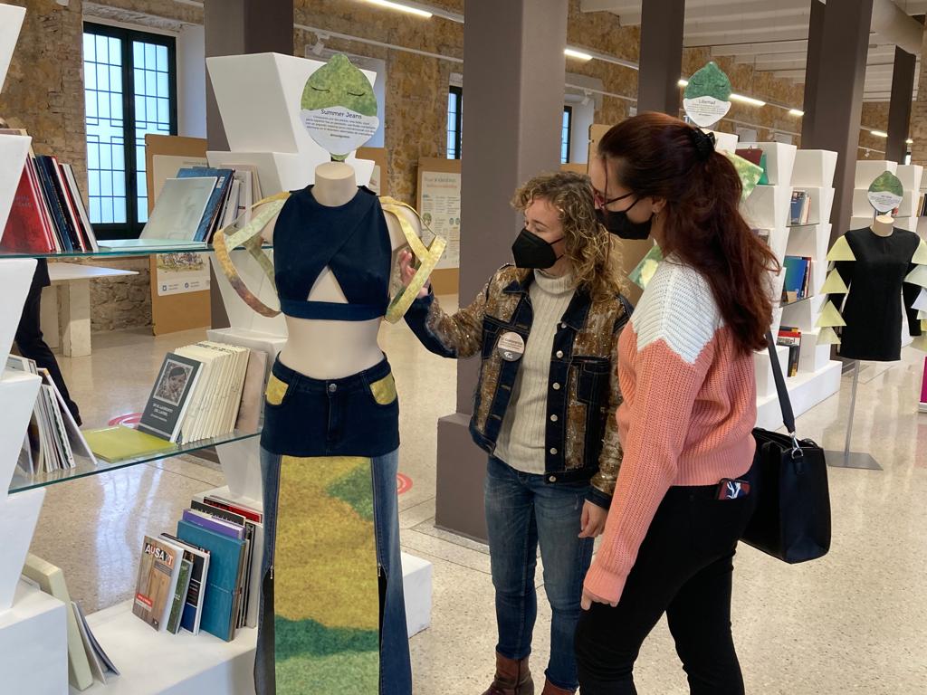 Dos chicas contemplan un vestido realizado con material reciclado que se expone en la muestra que se ha habilitado en el Pabellón 1 del Cuartel de Artillería de la calle Cartagena de Murcia