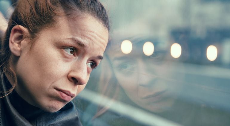 Imagen de una mujer triste frente al cristal de un autobús.