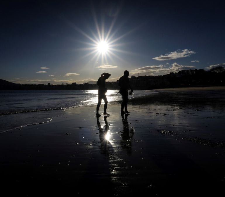 Dos hombres salen del agua al amanecer en la playa de Ondarreta de San Sebastián.