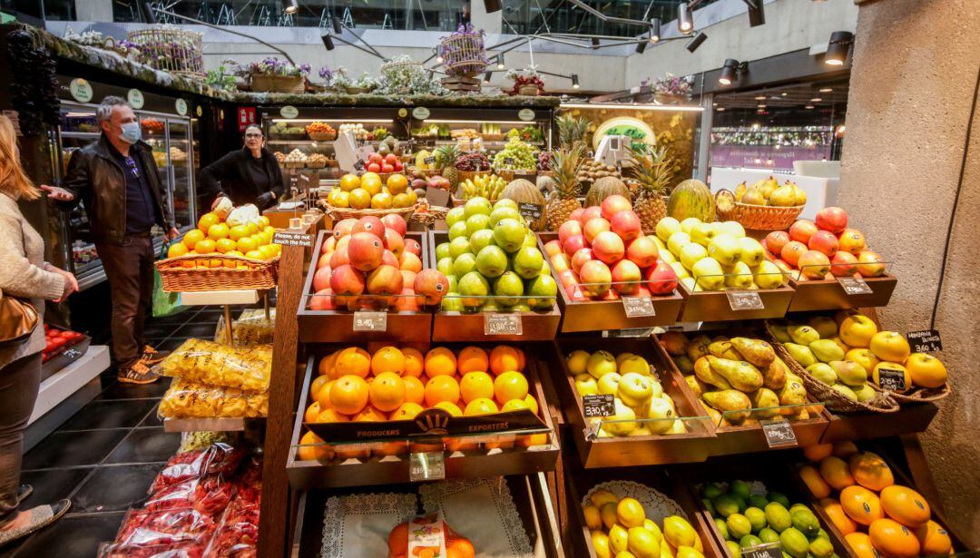 Varios clientes con mascarilla hacen la compra en un puesto de fruta en el mercado de San Antón, que permanece abierto en plena crisis del coronavirus y anuncia que también atiende a domicilio, en Madrid (España).