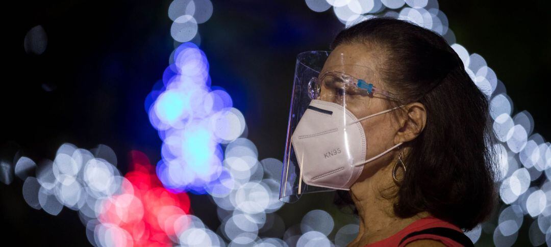 Una mujer con mascarilla y pantalla y luces de Navidad al fondo.