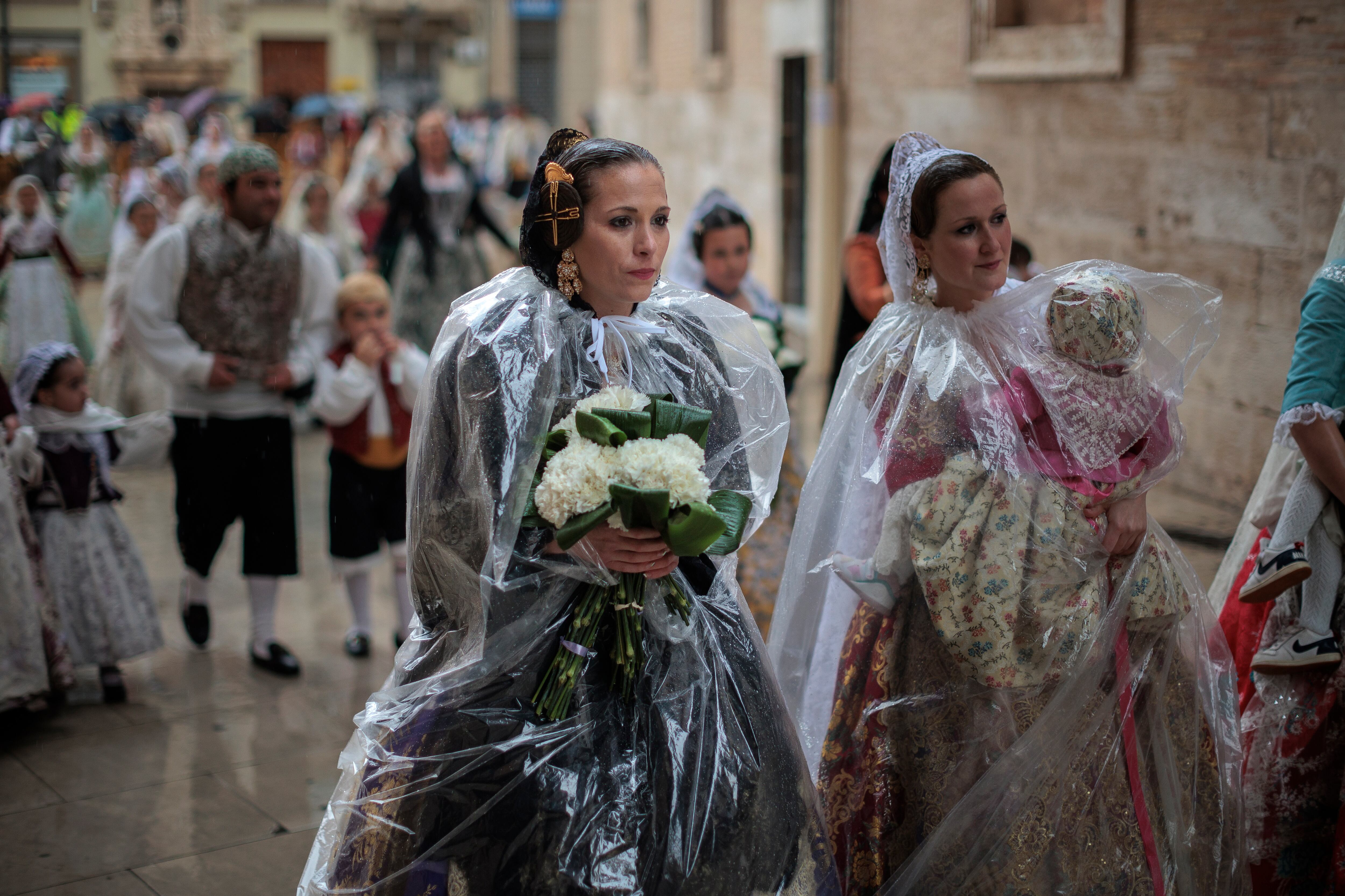 Unas falleras se protegen de la lluvia con chubasqueros durante el principal acto devoto de las Fallas, la Ofrenda floral a la Virgen de los Desamparados.