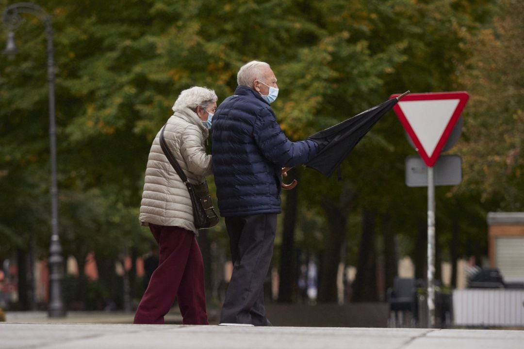 Una pareja de personas mayores, protegidas con mascarillas, pasea por la calle de una ciudad.