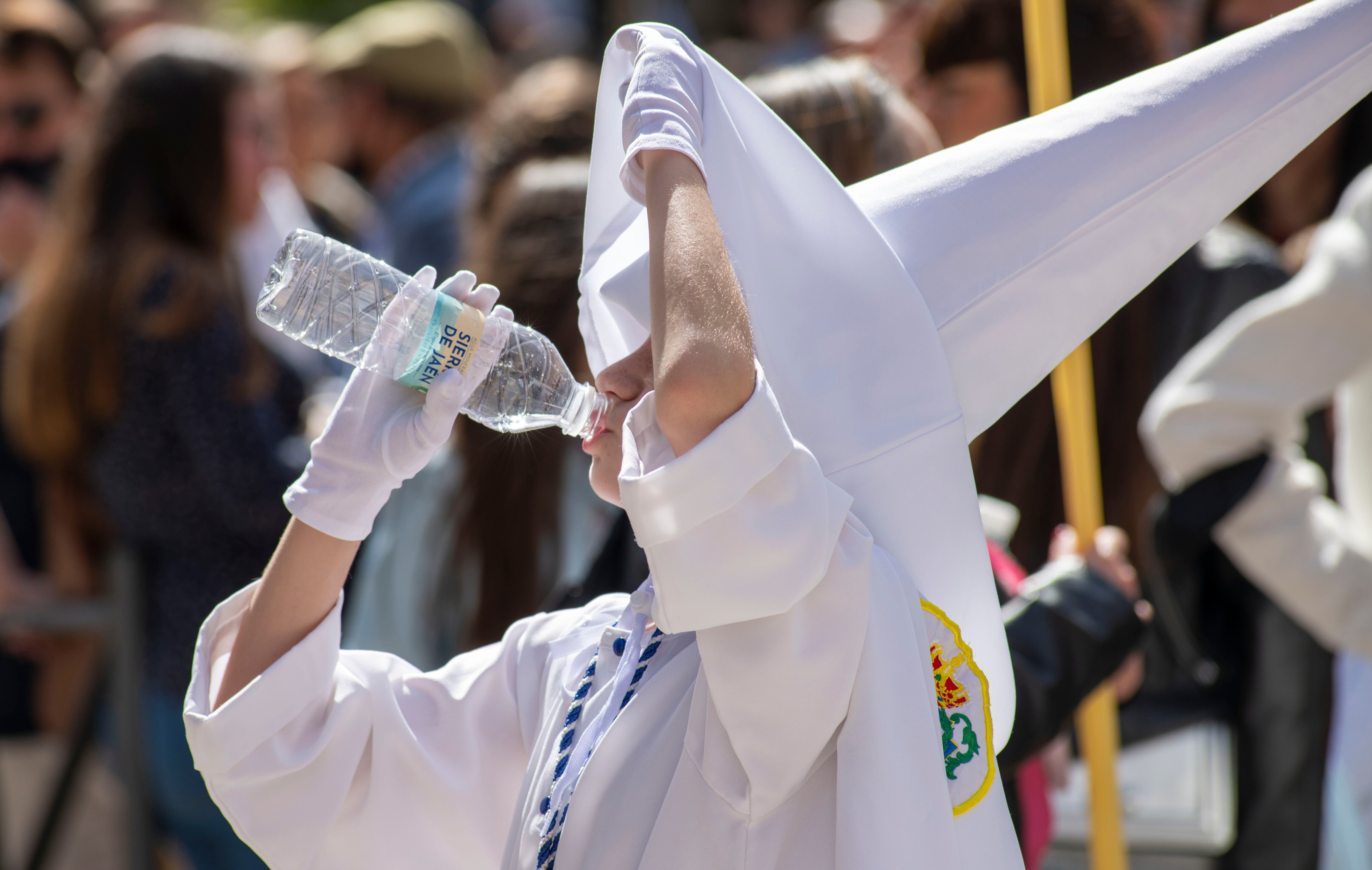 Un nazareno se refresca ante las altas temperaturas registradas en el primer día de la Semana Santa en Jaén, durante la procesión de la Borriquilla.