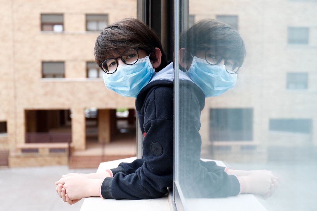 Un niño con una mascarilla se asoma a la ventana de su casa durante el confinamiento por el coronavirus.