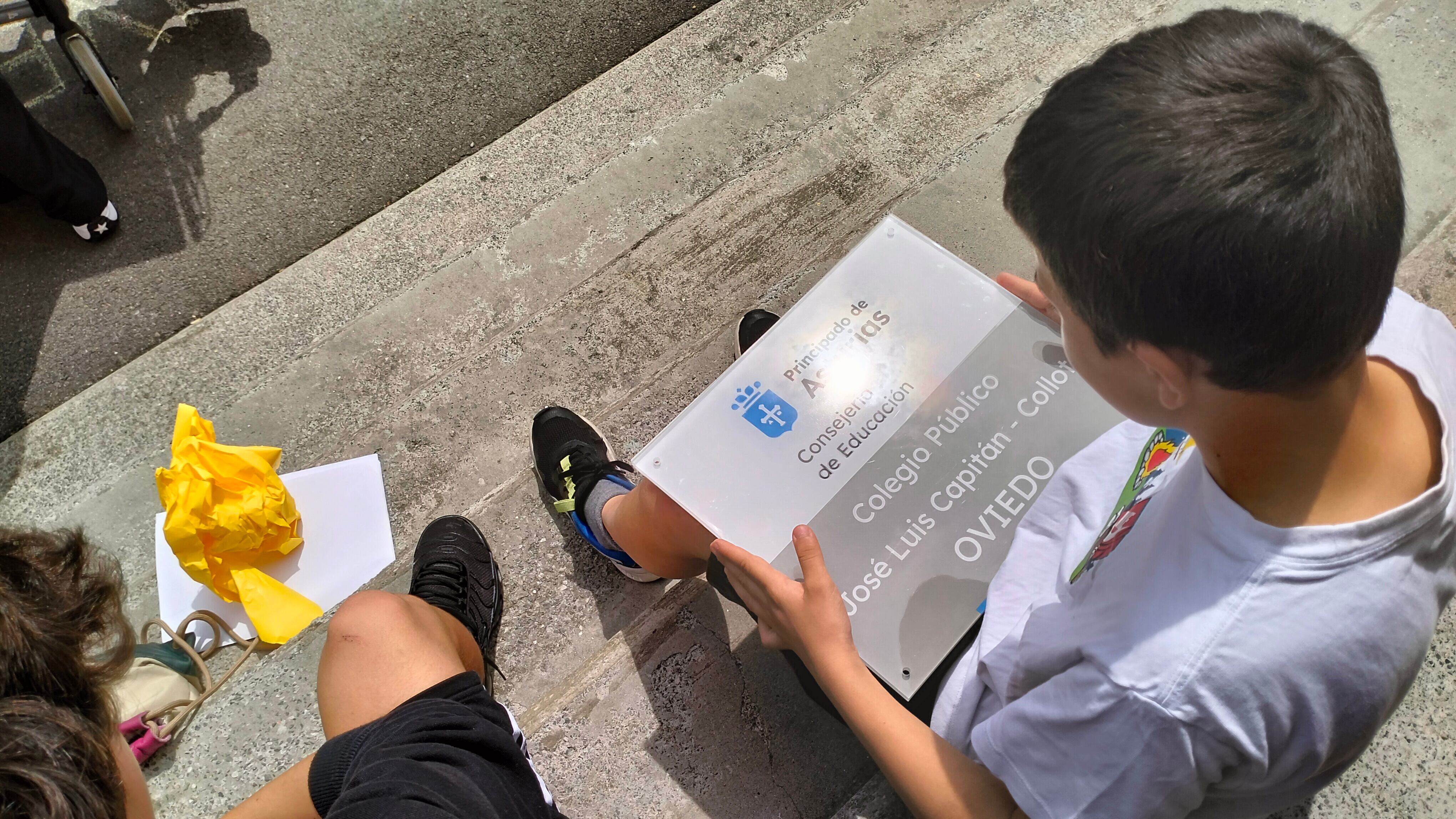 Uno de los hijos de "Capi" sostiene la copia de la placa instalada en la fachada del colegio que su familia se llevó para casa