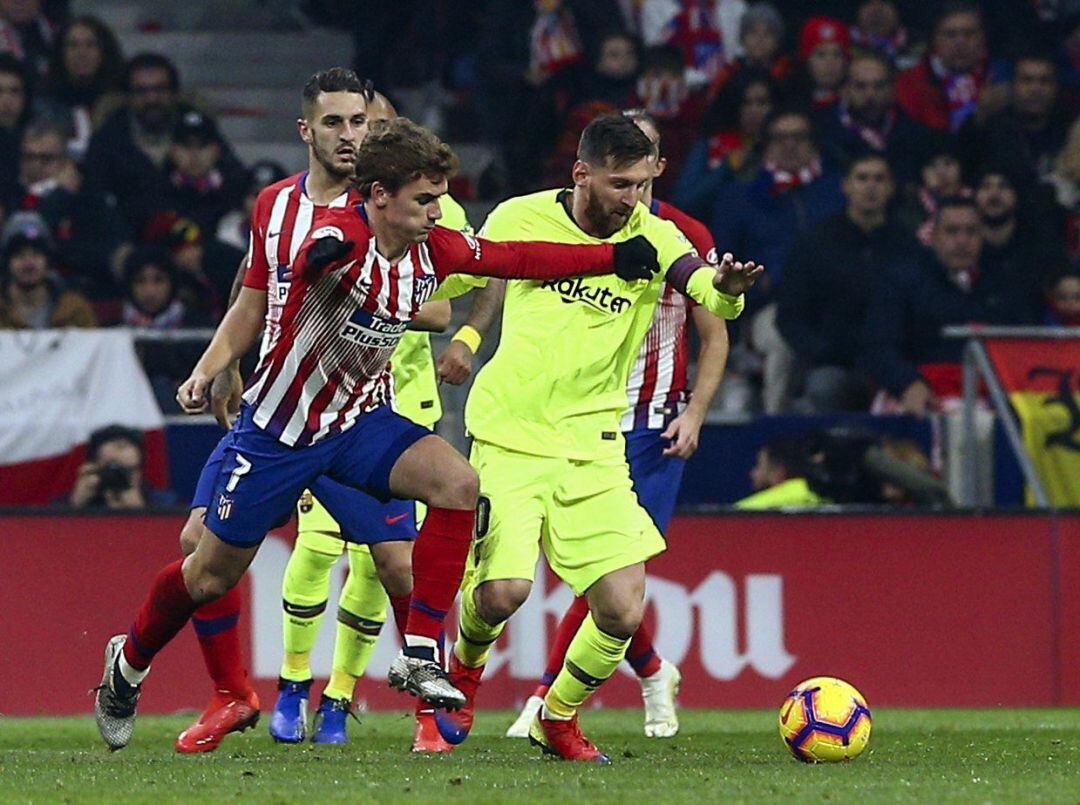 El delantero francés del Atlético de Madrid Griezmann (i) pelea un balón con Leo Messi, del FC Barcelona, durante el partido de Liga en Primera División que disputan esta noche en el estadio Metropolitano, en Madrid. 