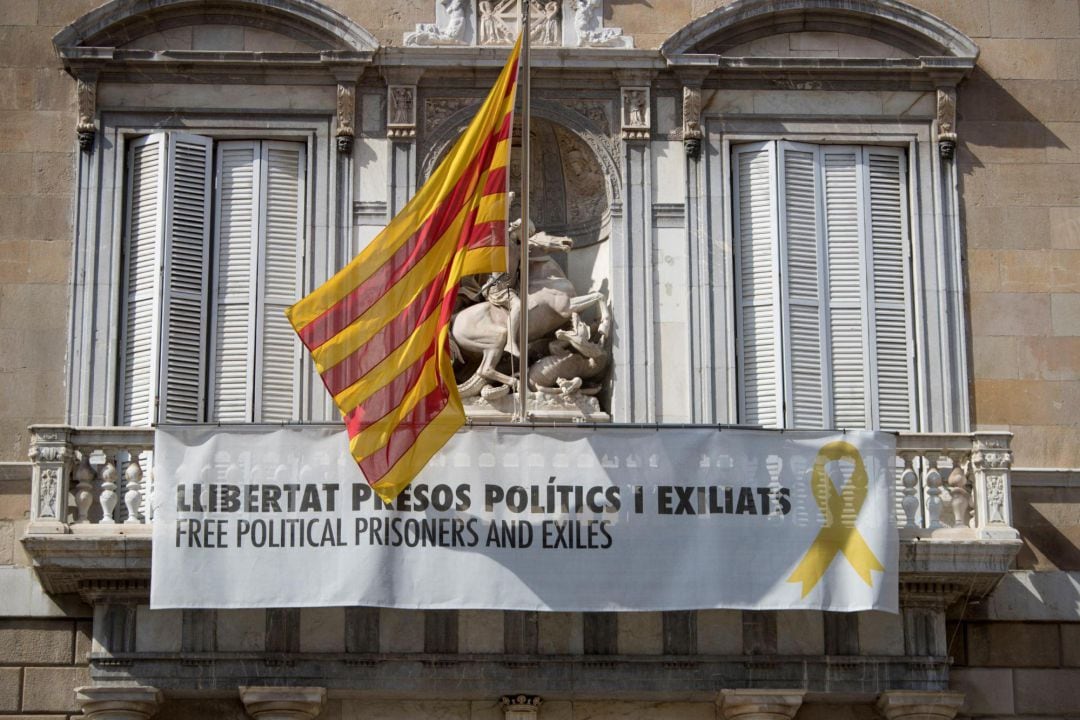 Vista de la fachada del Palau de la Generalitat de donde cuelga, junto a la bandera catalana, un cartel y un lazo amarillo reivindicando la libertad de los políticos encarcelados