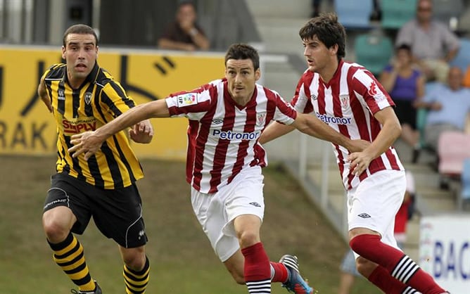 El delantero del Athletic Club de Bilbao, Aritz Aduriz y su compañero de equipo Mikel San José entran al remate con la oposición del defensa del Barakaldo Alberto González, durante el partido amistoso disputado en el campo de Lasesarre de Barakaldo.