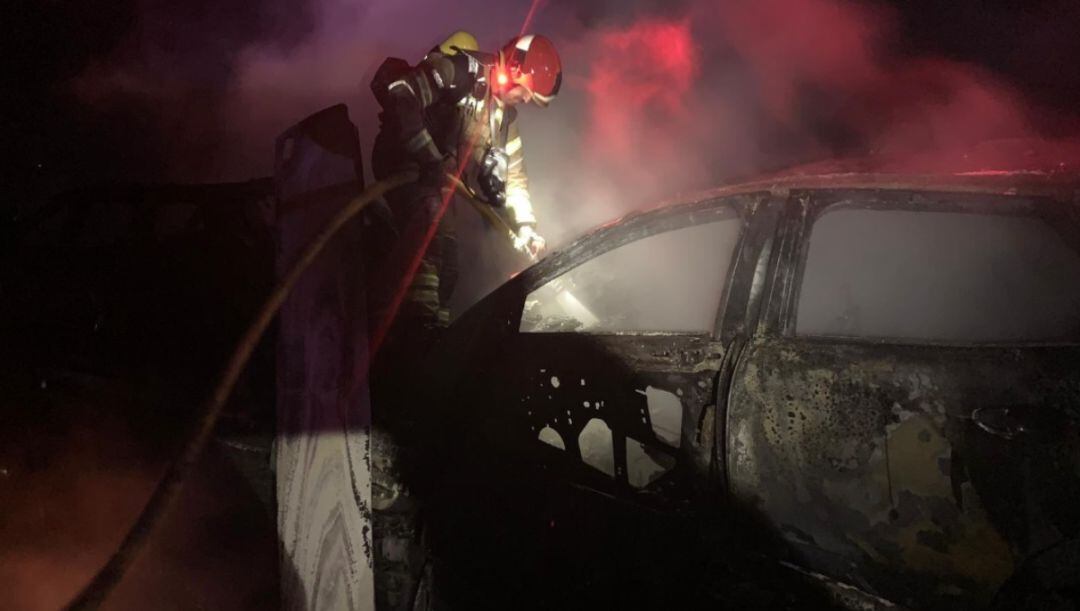 Un bombero apaga el incendio del vehículo siniestrado