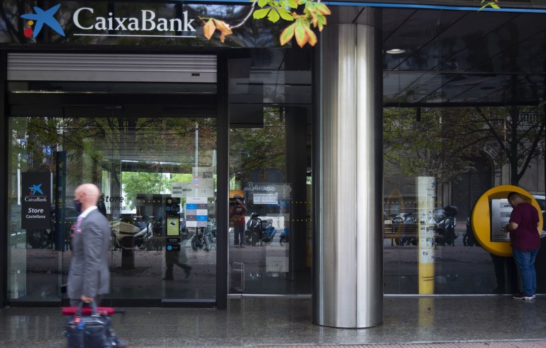 Varias personas frente a una sucursal de Caixabank.