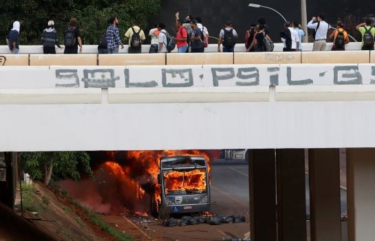 Varias personas observan el vehículo, quemado frente al Congreso, en Brasilia.