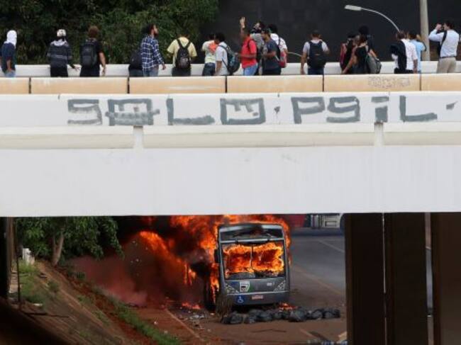 Varias personas observan el vehículo, quemado frente al Congreso, en Brasilia.
