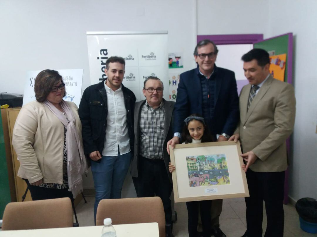 Foto de familia, Zaira Sánchez Liébana,  con una reproducción de su dibujo, acompañada de representantes del colegio, empresa, delegación y ayuntamiento