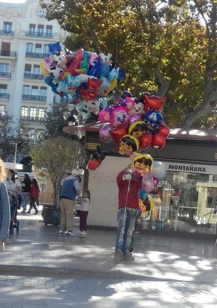 Un vendedor porta este domingo decenas de globos infantiles en la plaza del Ayuntamiento de València.