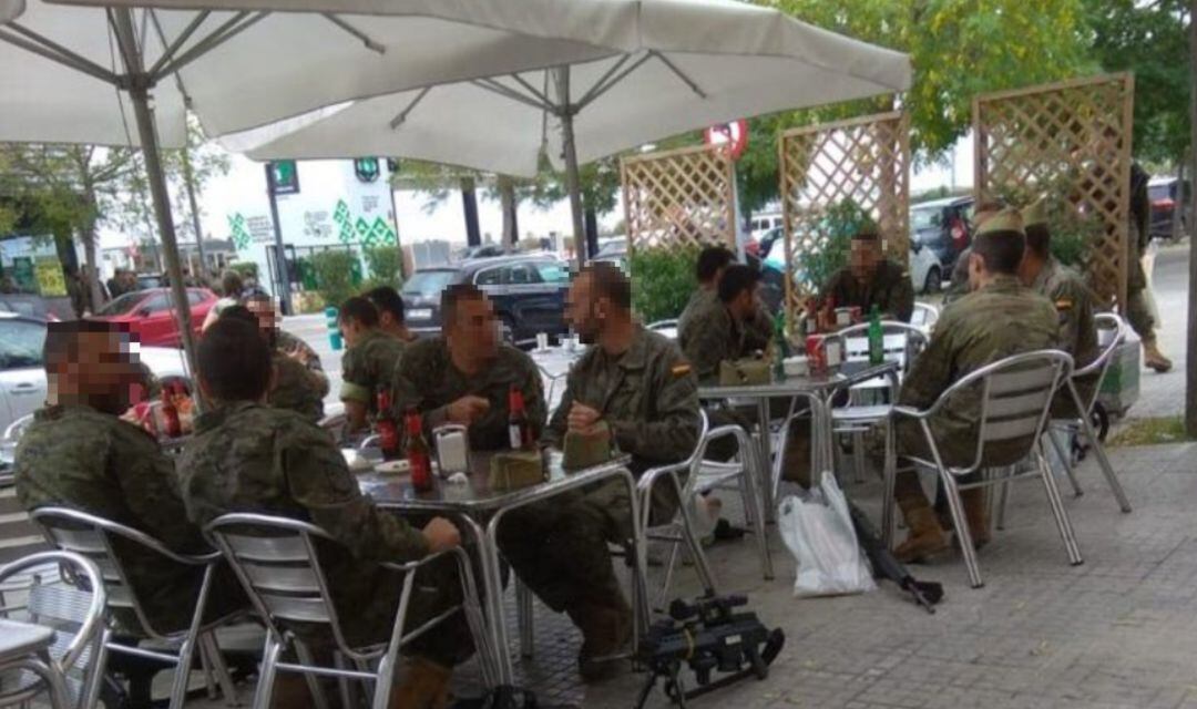 Un grupo de militares sentados en una terraza con armas largas en el suelo. 