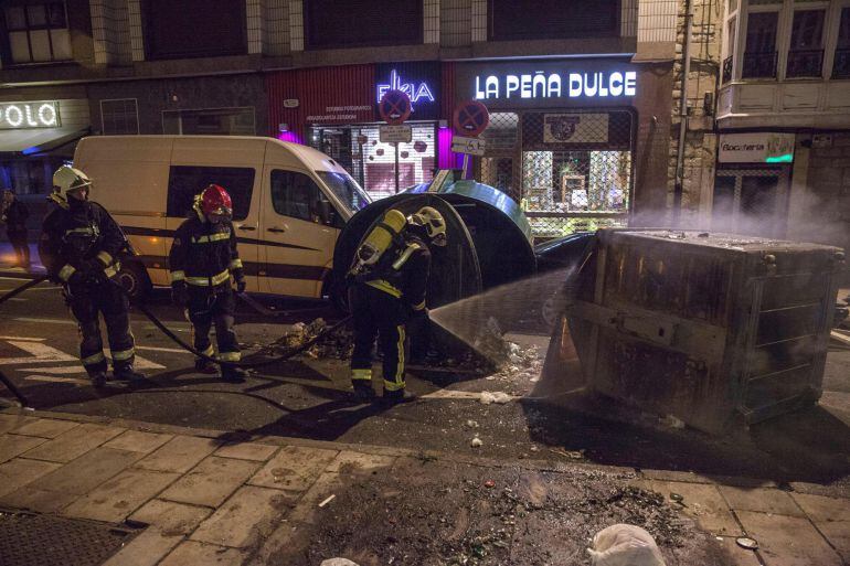 Los bomberos apagan un contenedor volcado e incendiado durante los incidentes en Vitoria