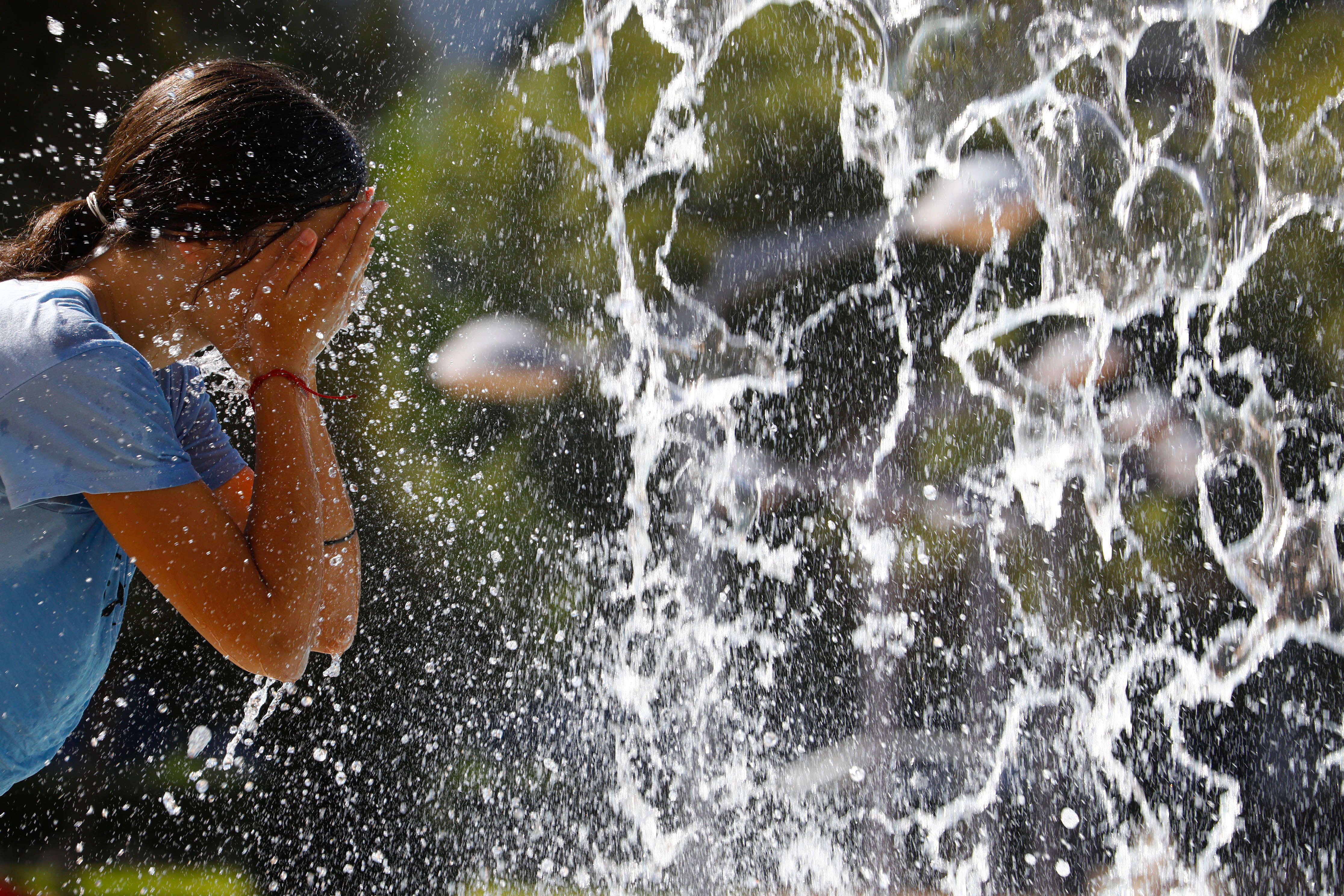 Una mujer se refresca en una fuente.