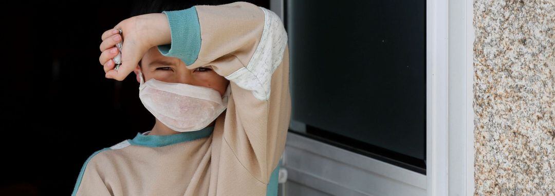 Un niño con una mascarilla casera a las puertas de su casa 