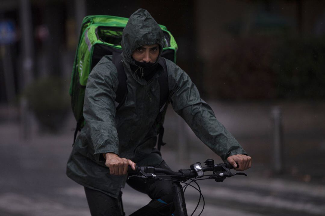 Un rider (repartidor) trabaja bajo la lluvia protegido con un impermeable. En Sevilla.