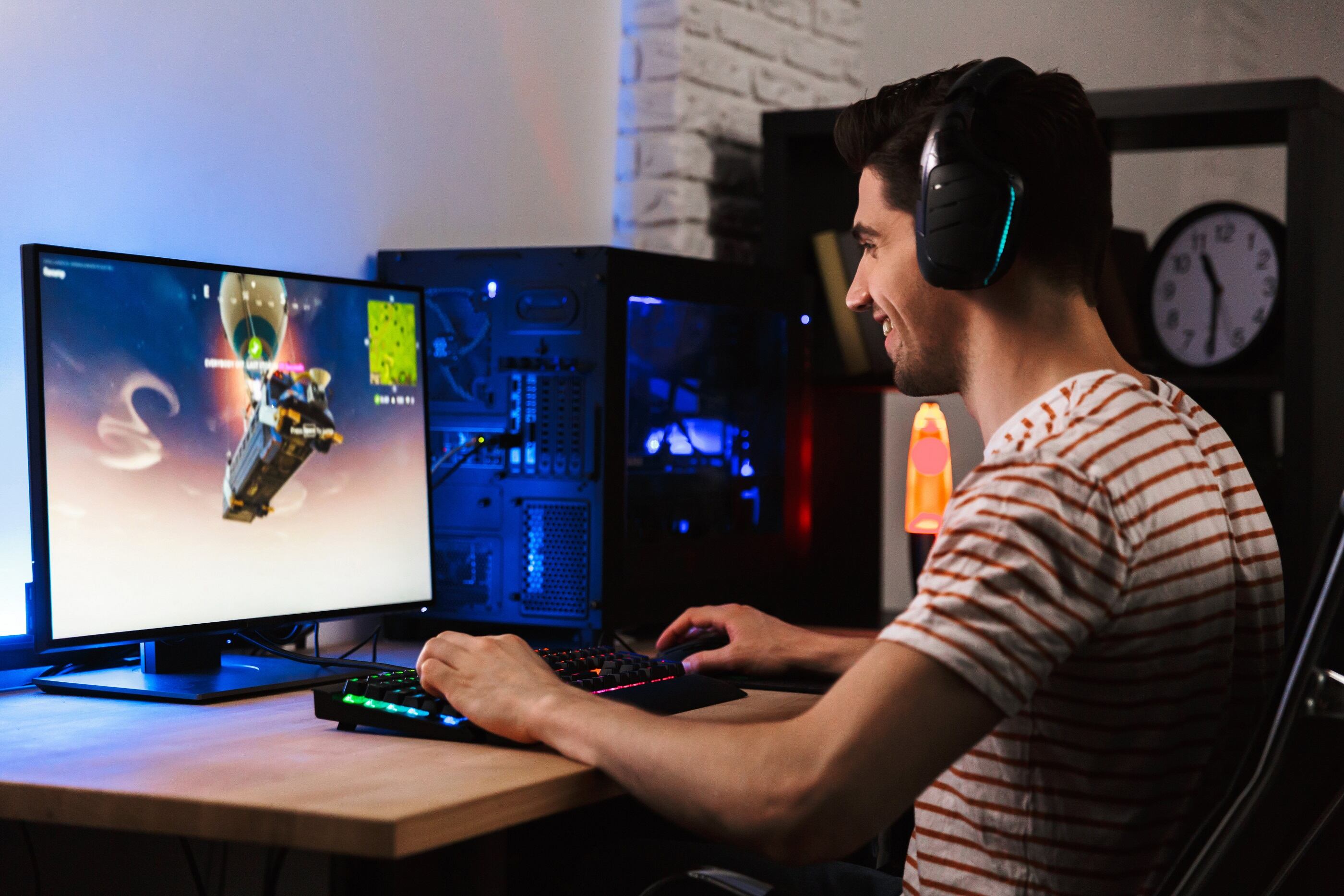Portrait of young gamer man playing video games on computer wearing headphones and using backlit colorful keyboard