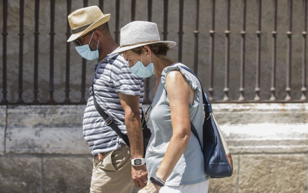Dos personas caminan con mascarilla y sombrero.