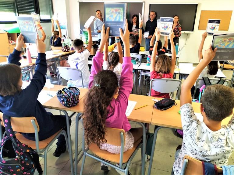 Alumnos en clase levantan sus cuadernos