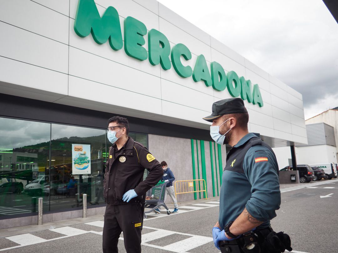 Un agente de la Guardia Civil y otro agente de seguridad privada, frente a la puerta de un gran supermercado durante el periodo de estado de alarma en España.