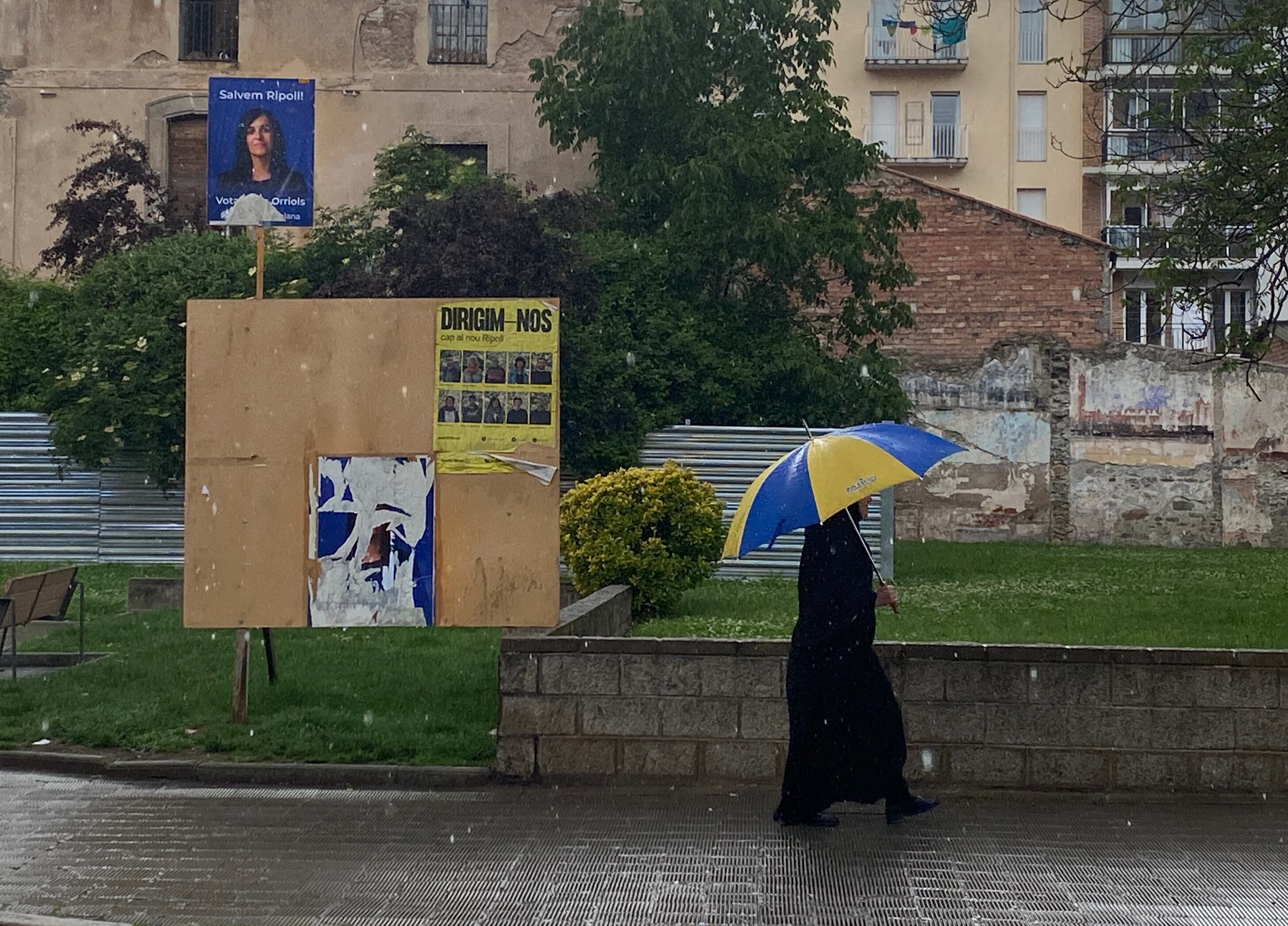 Una mujer vestida con burka pasa por delante de varios cateles electorales, entre ellos el de Aliança Catalana.