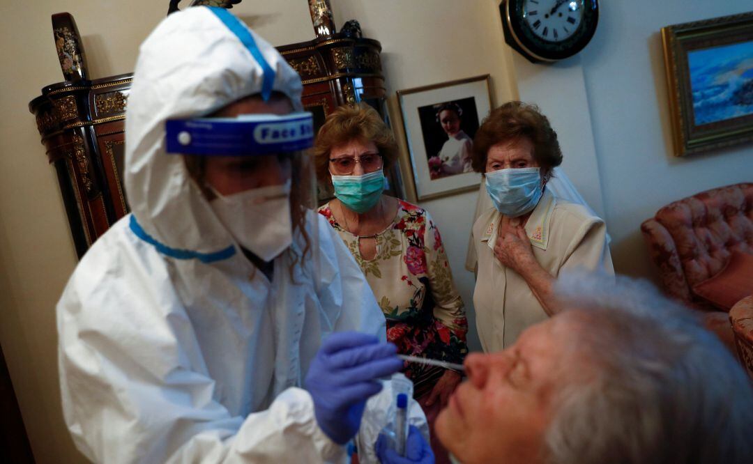 Una saniraria realiza una prueba de Covid-19 a una mujer en presencia de otras dos.