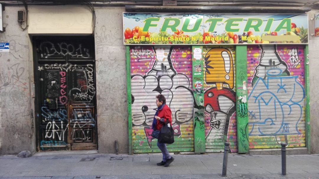 Una mujer pasa por delante de un portal y un comercio llenos de pintadas y firmas en Malasaña.