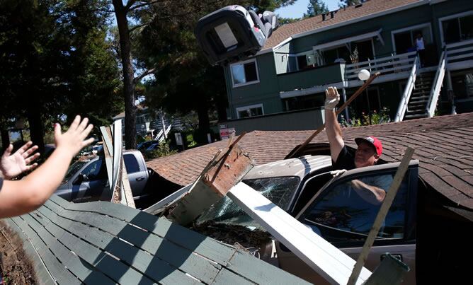 Un hombre saca un asiento de un coche destrozado tras caerle encima una vivienda en la localidad californiana de Napa.