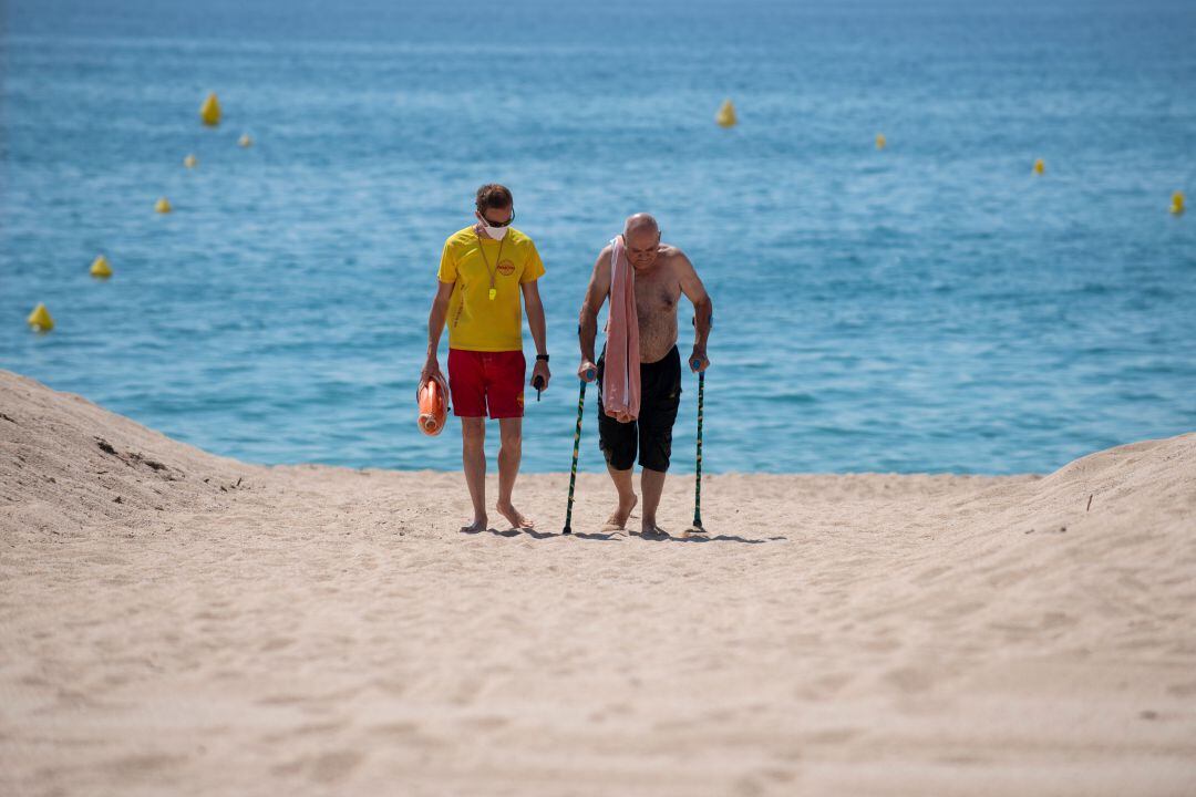 Un socorrista ayuda a un anciano a salir de la playa.